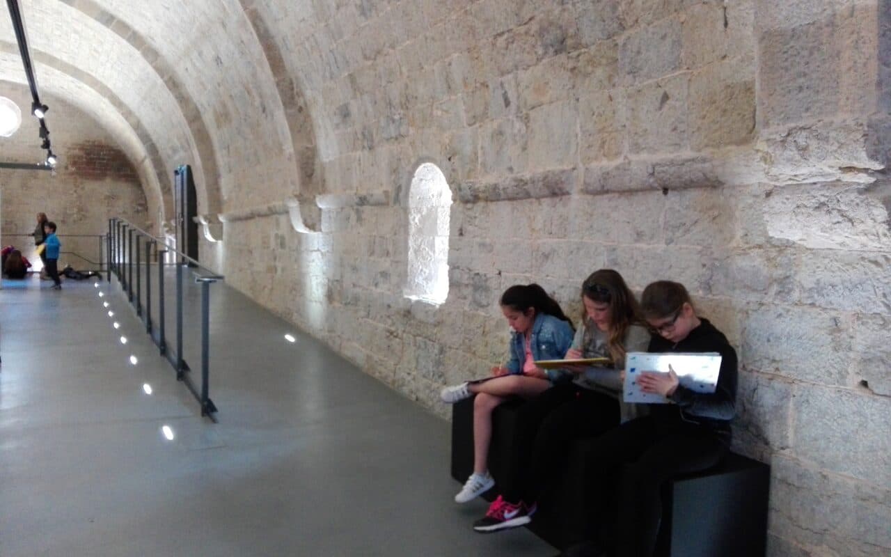 Trois enfants qui dessinent sur un banc dans une salle voutée de l'abbaye du Thoronet