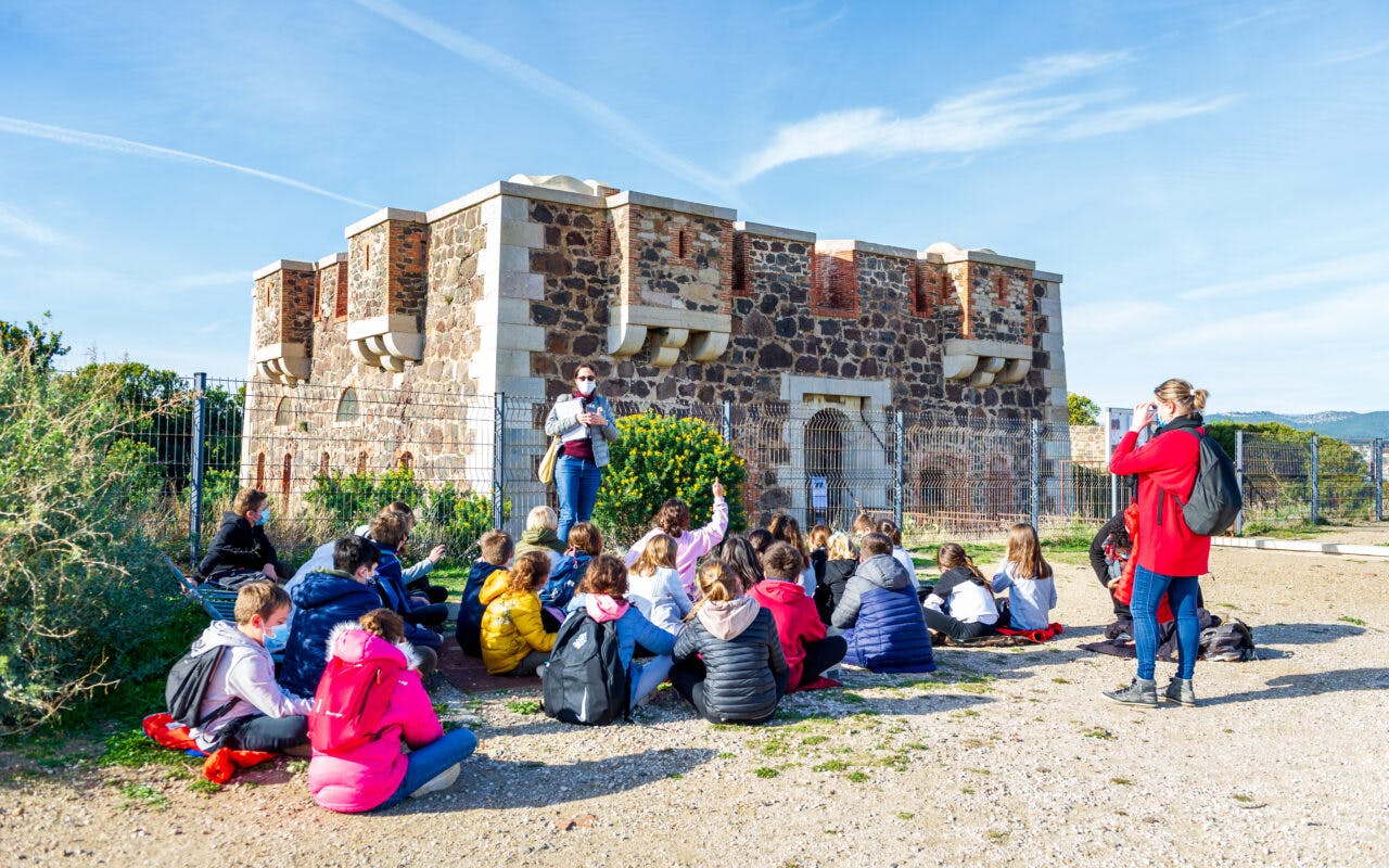 Groupe d'enfants assis face au patrimoine fortifié de la batterie du Cap Nègre à Six-Fours